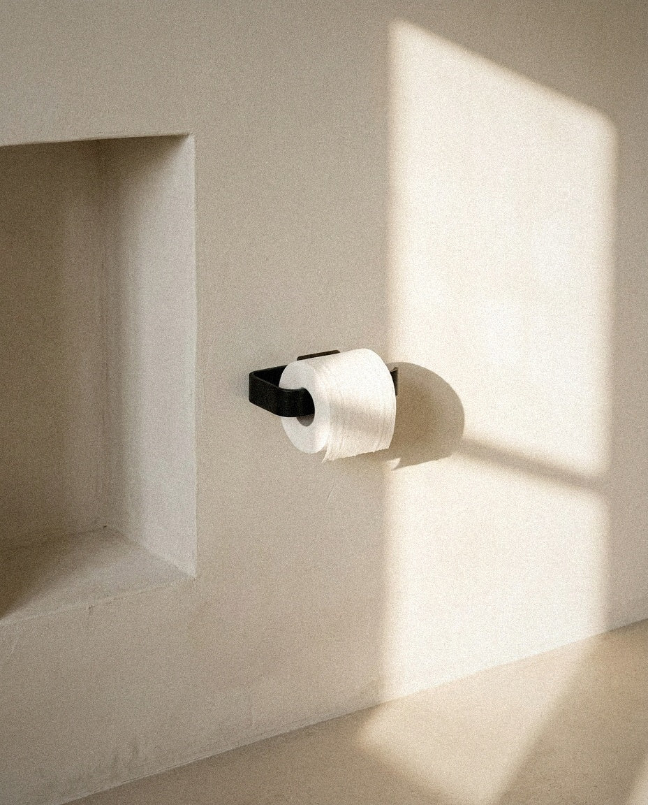 Matte black self-adhesive toilet paper holder on a warm plaster wall