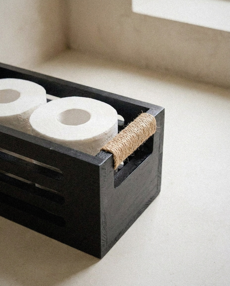 Close-up of the slotted black wood basket and jute rope handle with toilet rolls