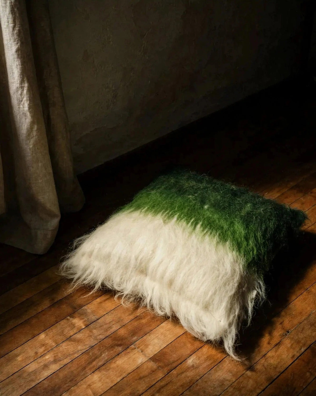 Emerald green handwoven wool pillow in mid-century modern interior, moody chiaroscuro light, editorial still life