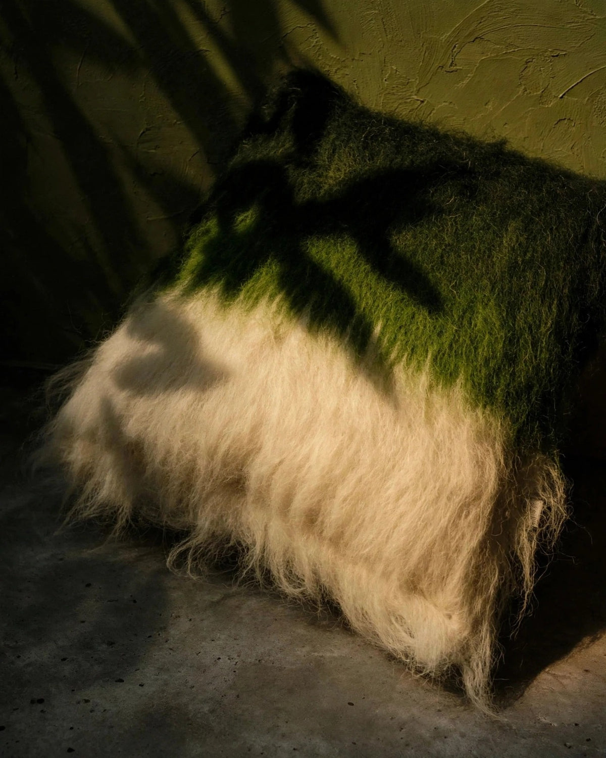 Emerald green handwoven wool pillow in organic modern interior, moody chiaroscuro light, editorial still life