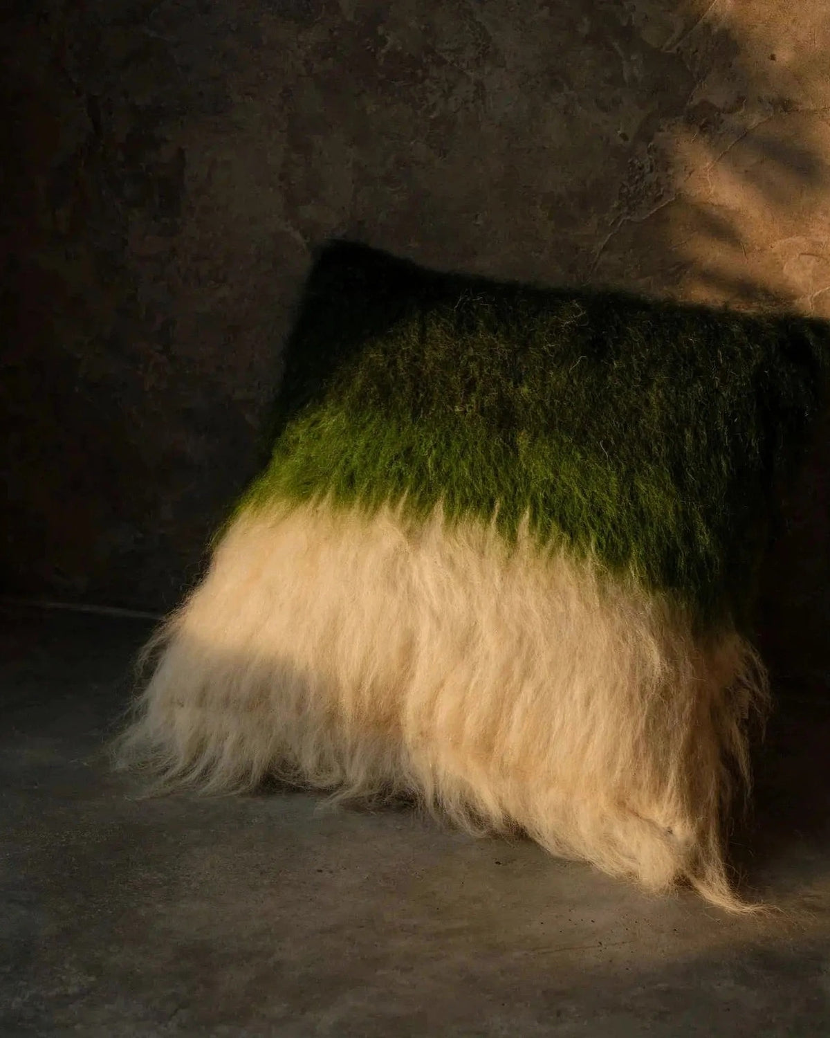 Emerald green handwoven wool pillow in organic modern interior, warm tungsten evening light, editorial still life