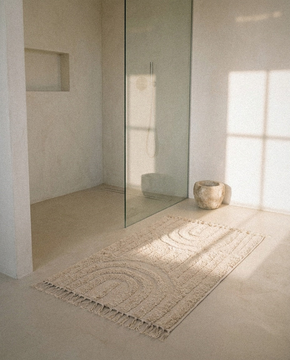 Hana cream arch-pattern bath mat with tassels in a calm tiled bathroom