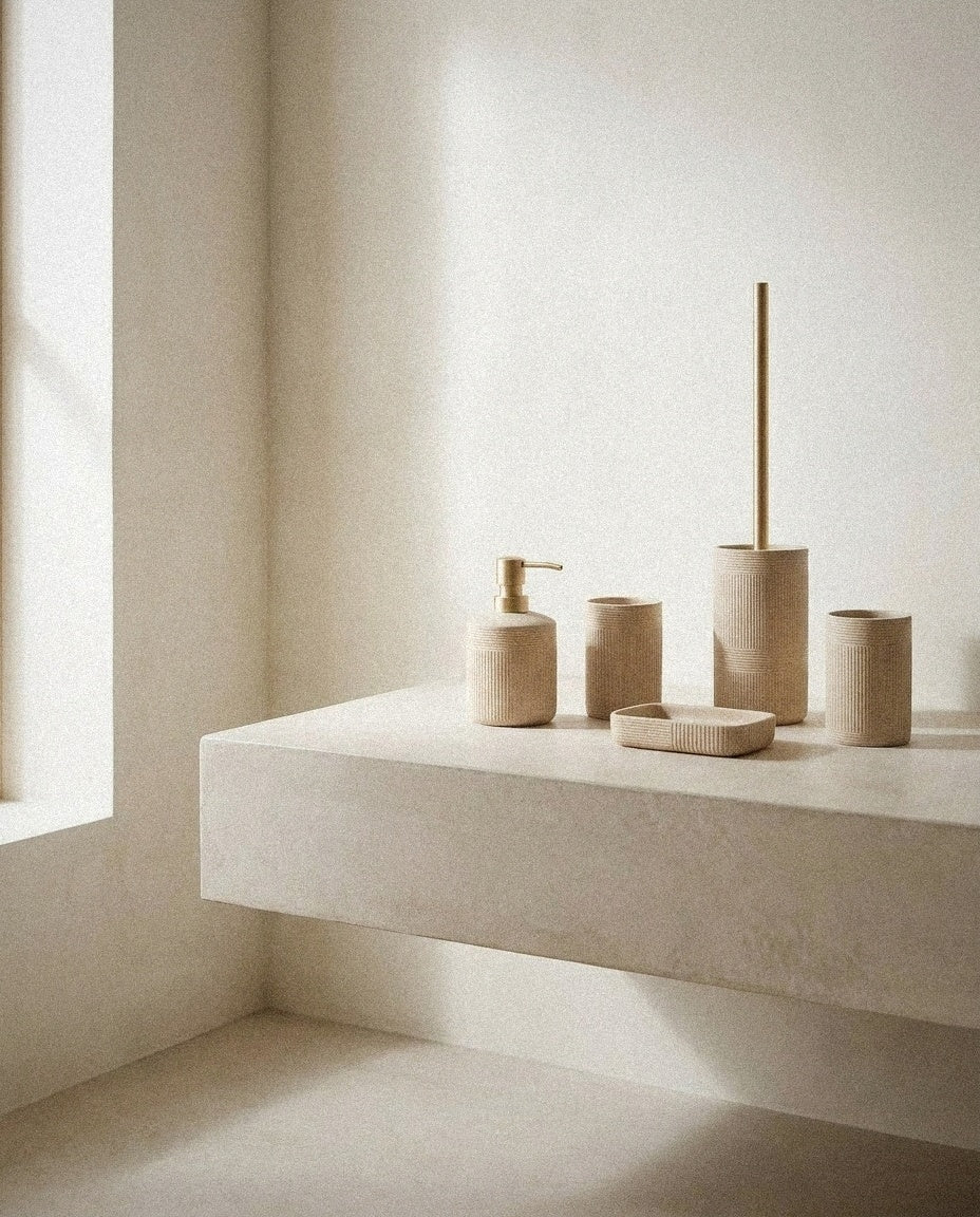 Beige ceramic bath set with soap dispenser, tumbler, soap dish and toilet brush on a plaster ledge