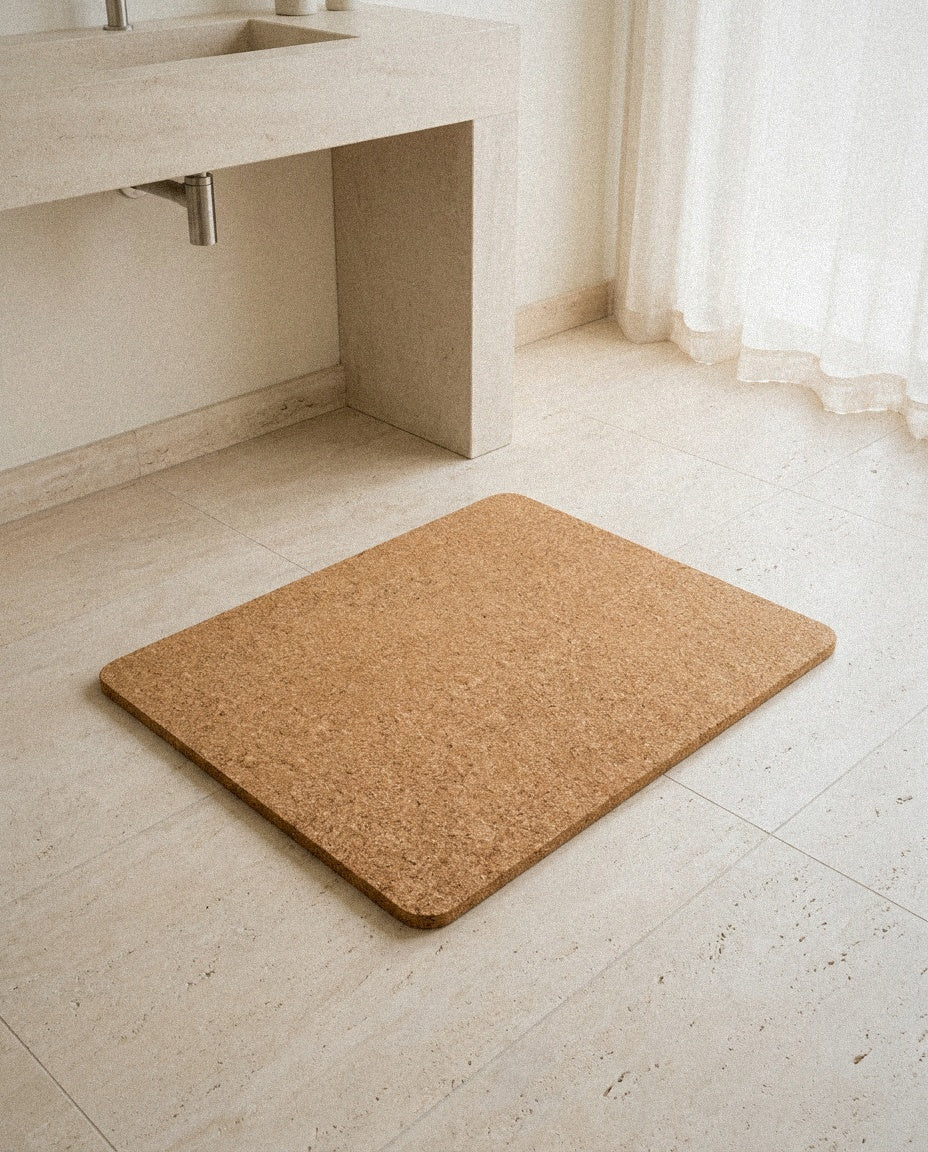Natural cork bath mat with rounded corners on a light travertine bathroom floor