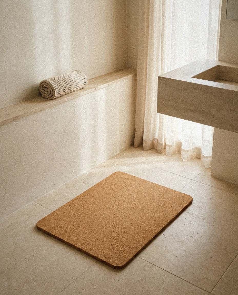 Cork bath mat in front of a limestone washbasin in a bright minimal bathroom