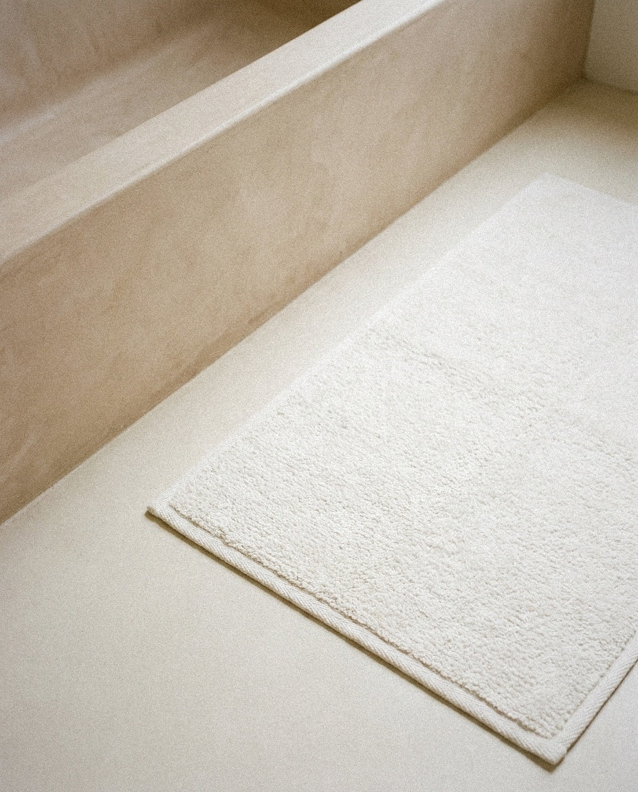 Close-up of the dense white terry loops and knit border of the organic bath mat