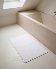 White organic Turkish cotton bath mat with double-knit border on a pale stone bathroom floor