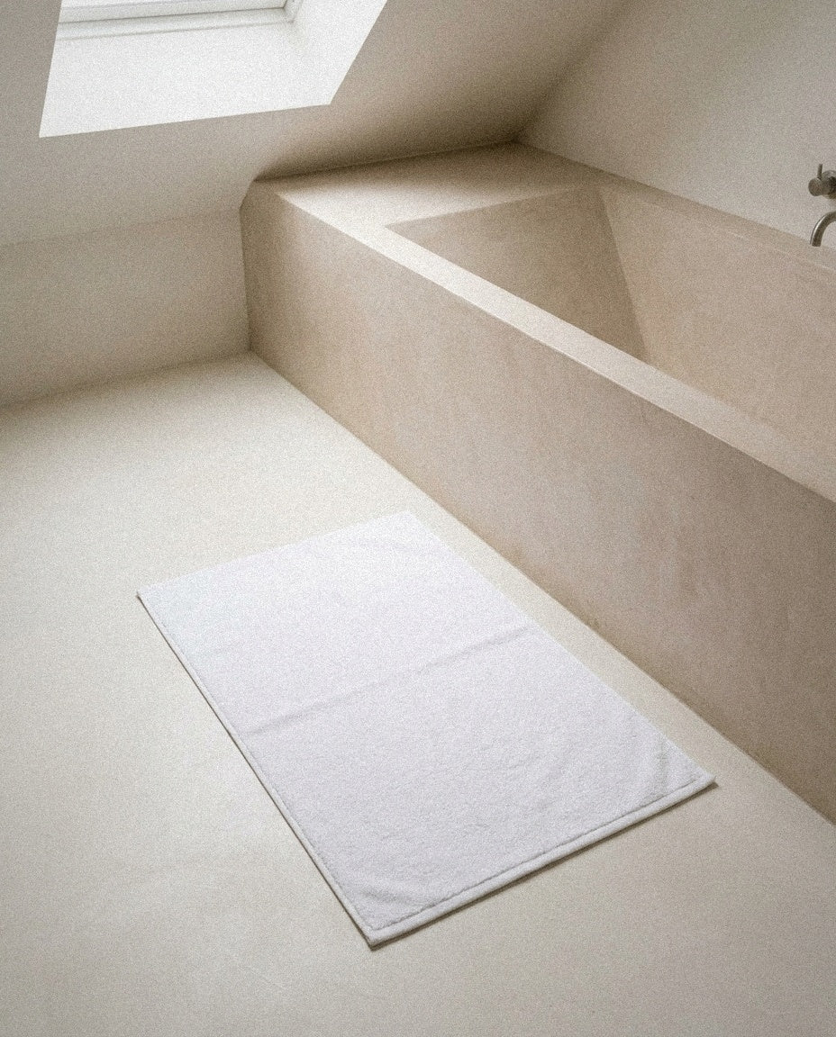 White organic Turkish cotton bath mat with double-knit border on a pale stone bathroom floor
