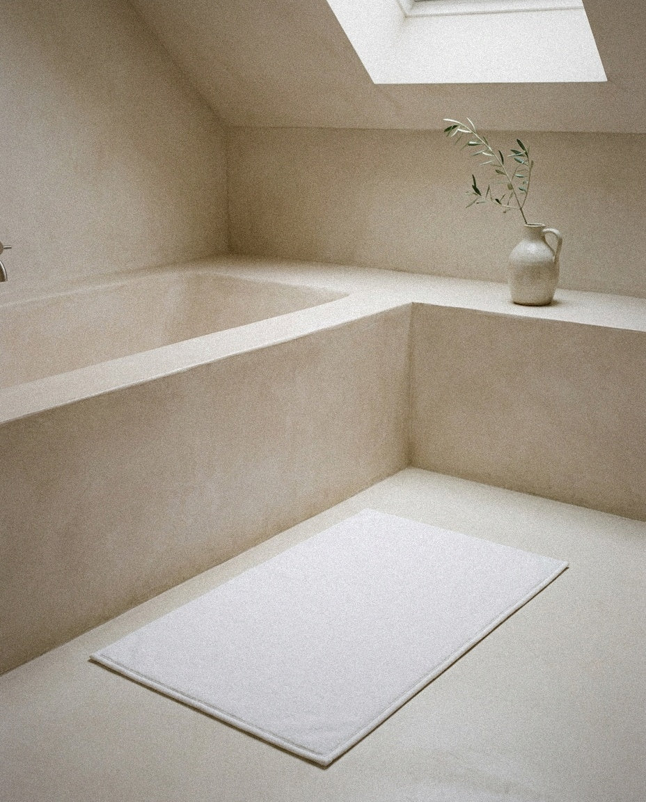 Organic cotton bath mat beside a built-in plaster bathtub in a minimal bathroom