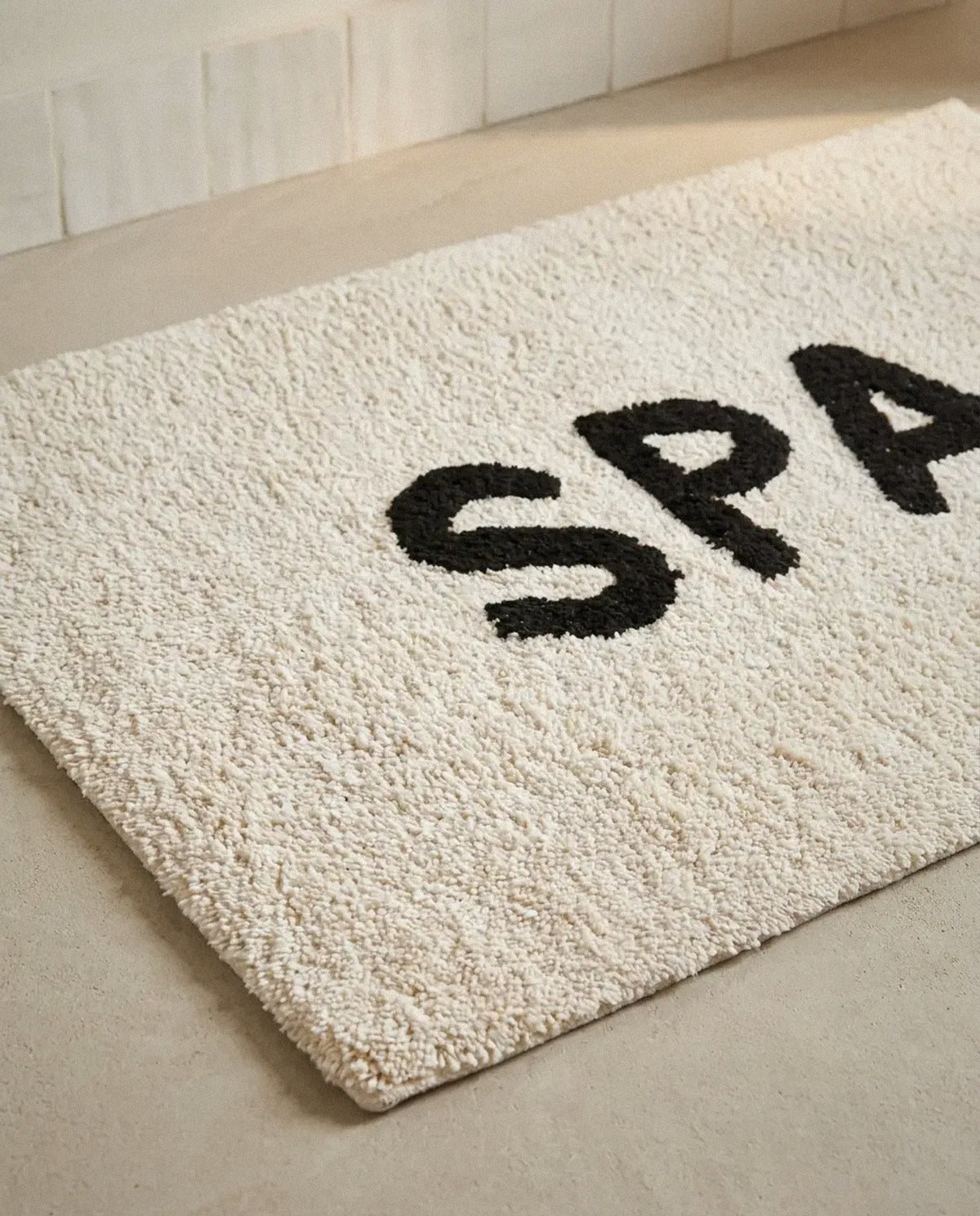 Close-up of the soft ivory tufted cotton pile and black SPA lettering of the bath mat