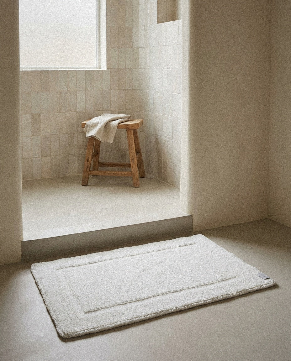 Plush white bath mat at the exit of a curved plaster wet-room shower