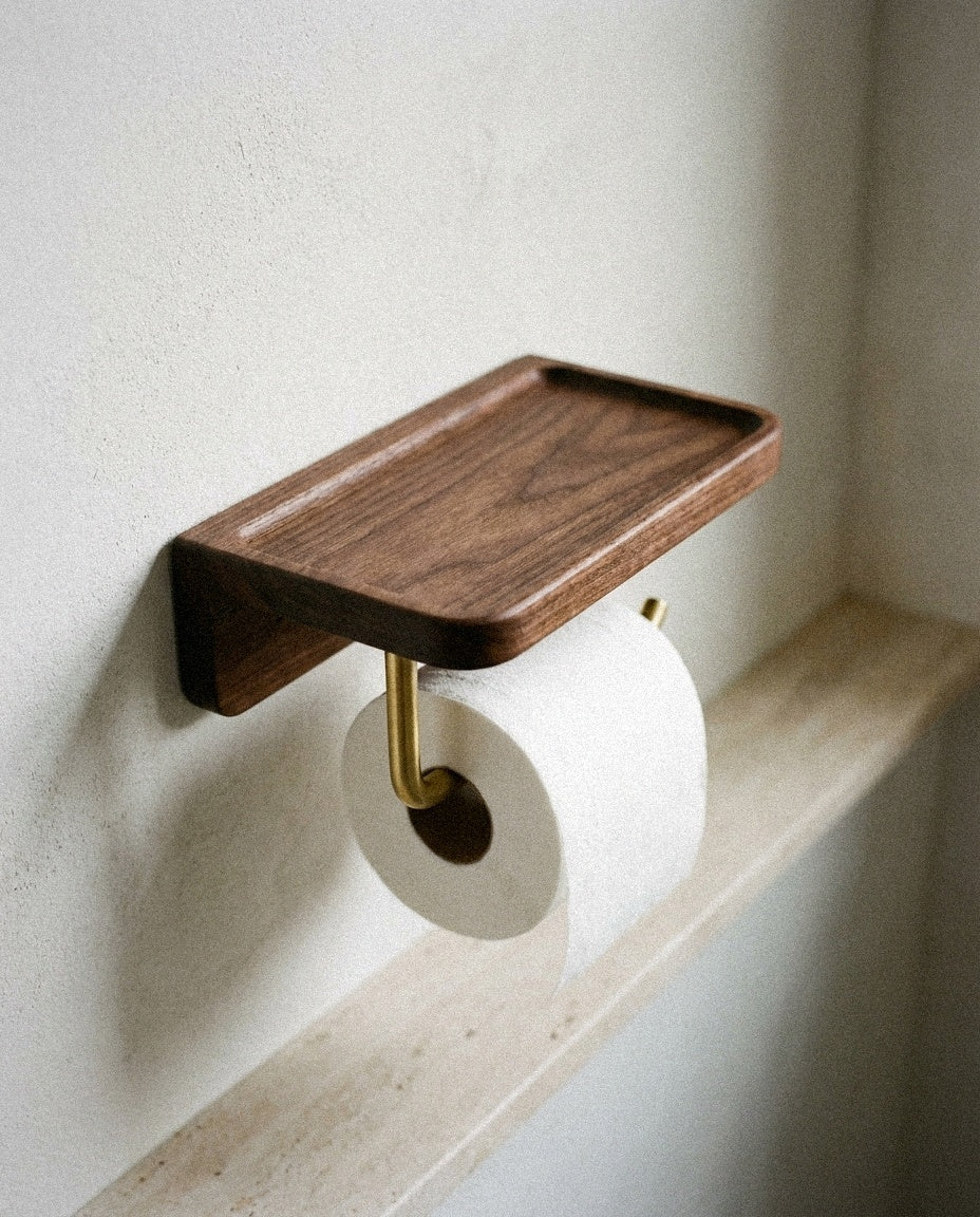 Close-up of the walnut shelf and brass roll arm of the toilet paper holder